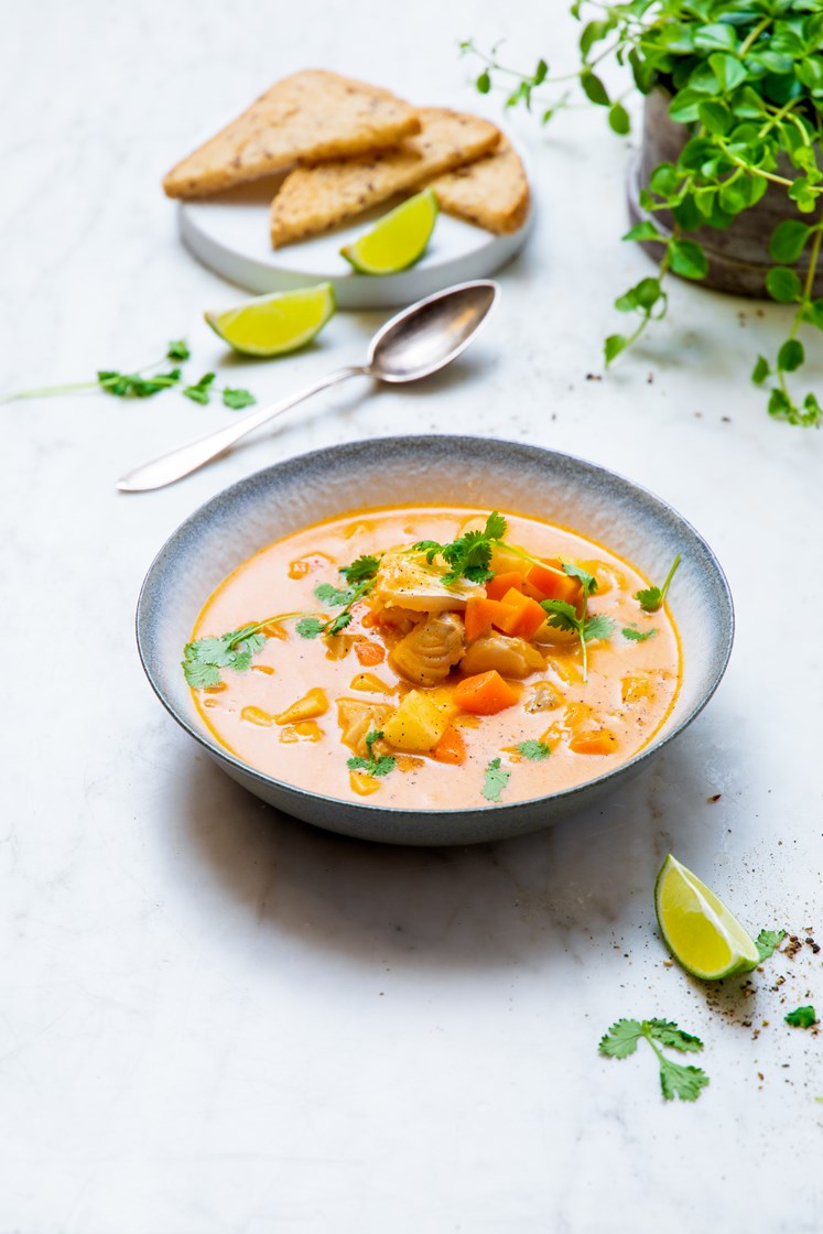 Rød currysuppe med fisk og grønnsaker servert med glutenfritt brød ...