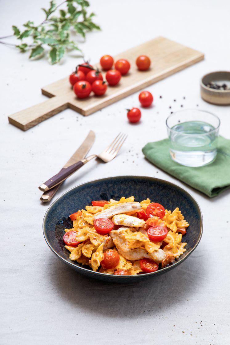 Skivet kyllingfilet og pasta farfalle i kremet paprikapesto, toppet med tomat
