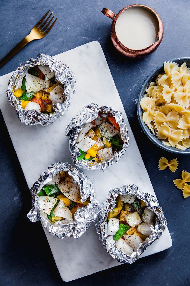 Fiskepakker med laks og torsk, fargerike grønnsaker, pasta og kremet fiskesaus