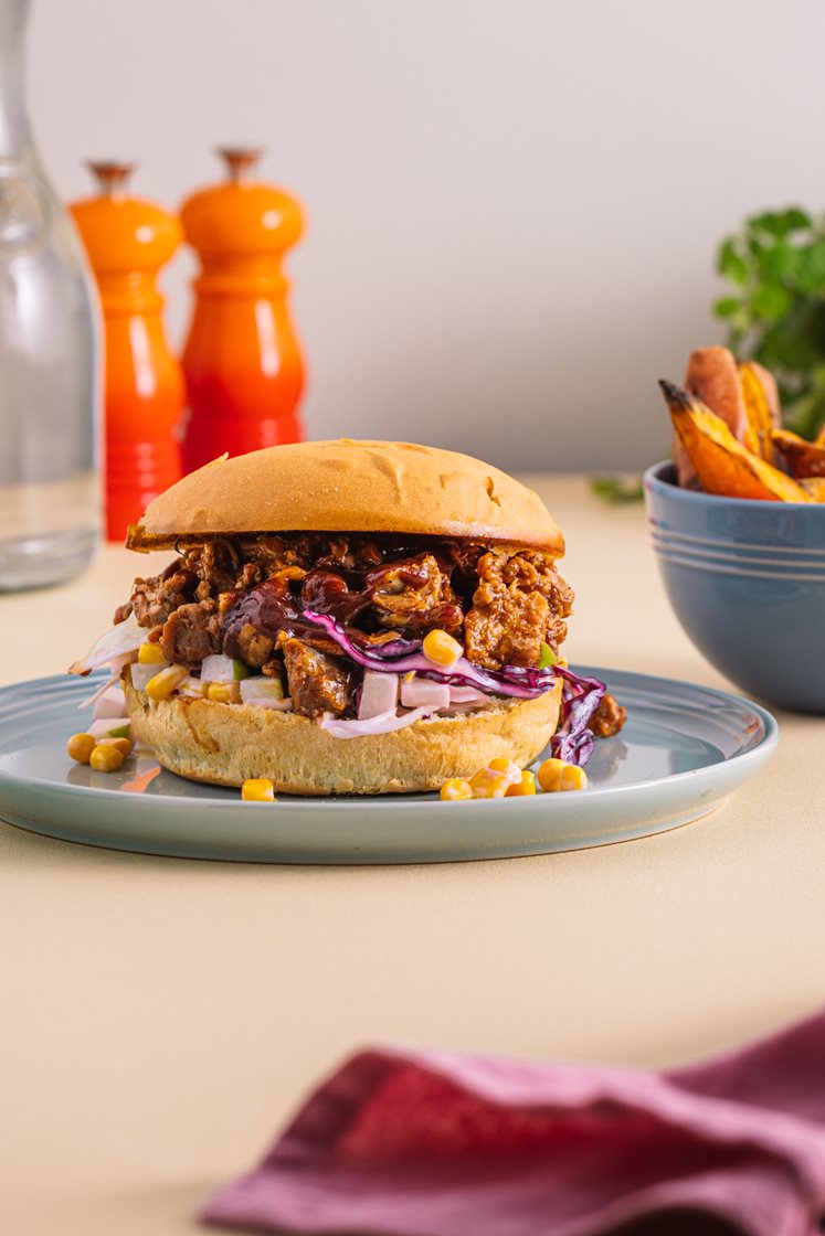 Pulled pork-burger med barbecuesaus, servert med maiscoleslaw og ovnsbakte søtpotetbåter