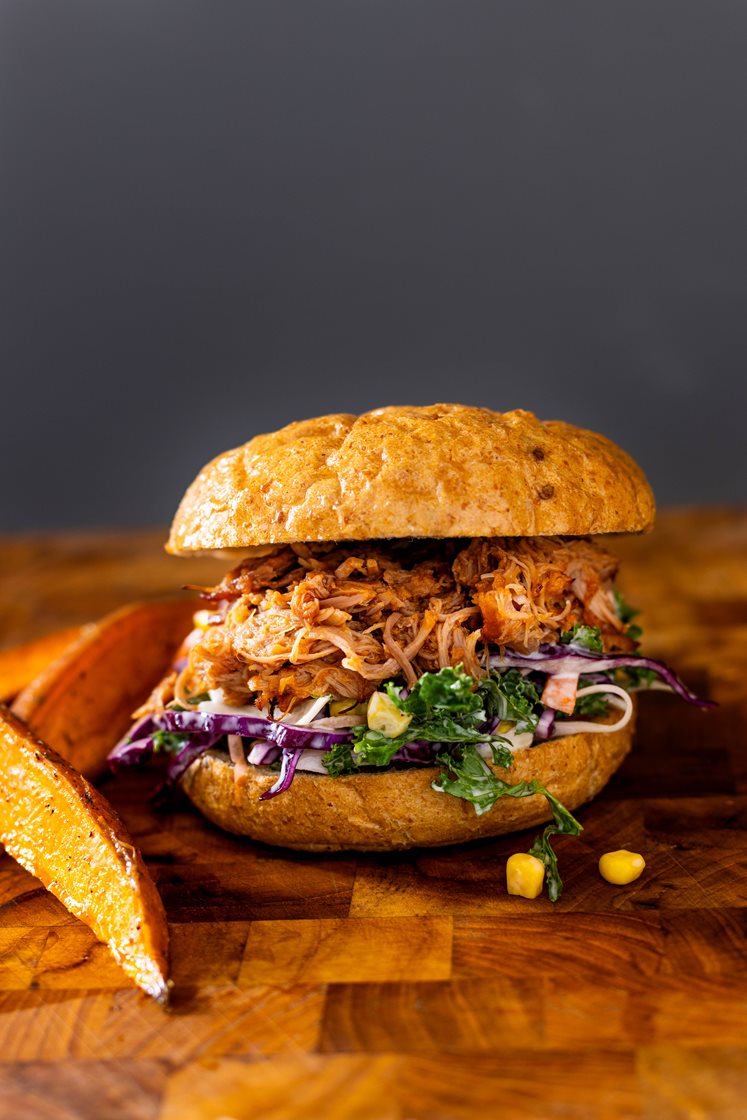 Pulled pork-burger med barbecuesaus, servert med maiscoleslaw og ovnsbakte søtpotetbåter