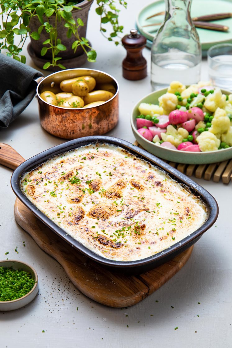 Gratinerte fiskeboller i hvit saus med blomkål, grønne erter og gressløk