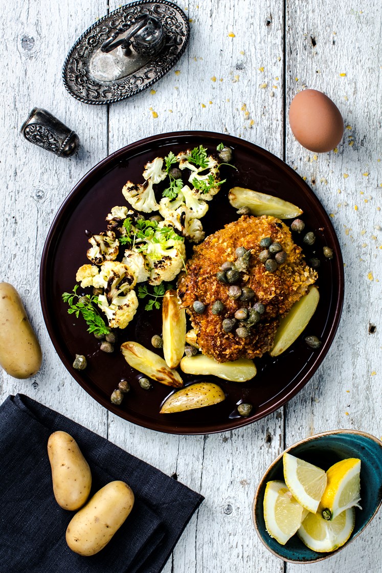 Hjemmelagde svineschnitzler med ovnsbakte potetbåter og blomkål, grønne erter og kaperssmør