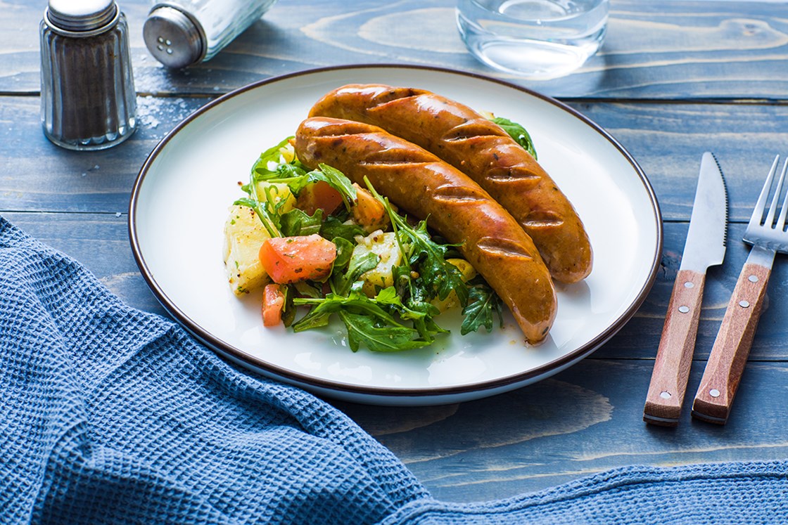 To sorter pølser servert med potetsalat med tomat og spinat