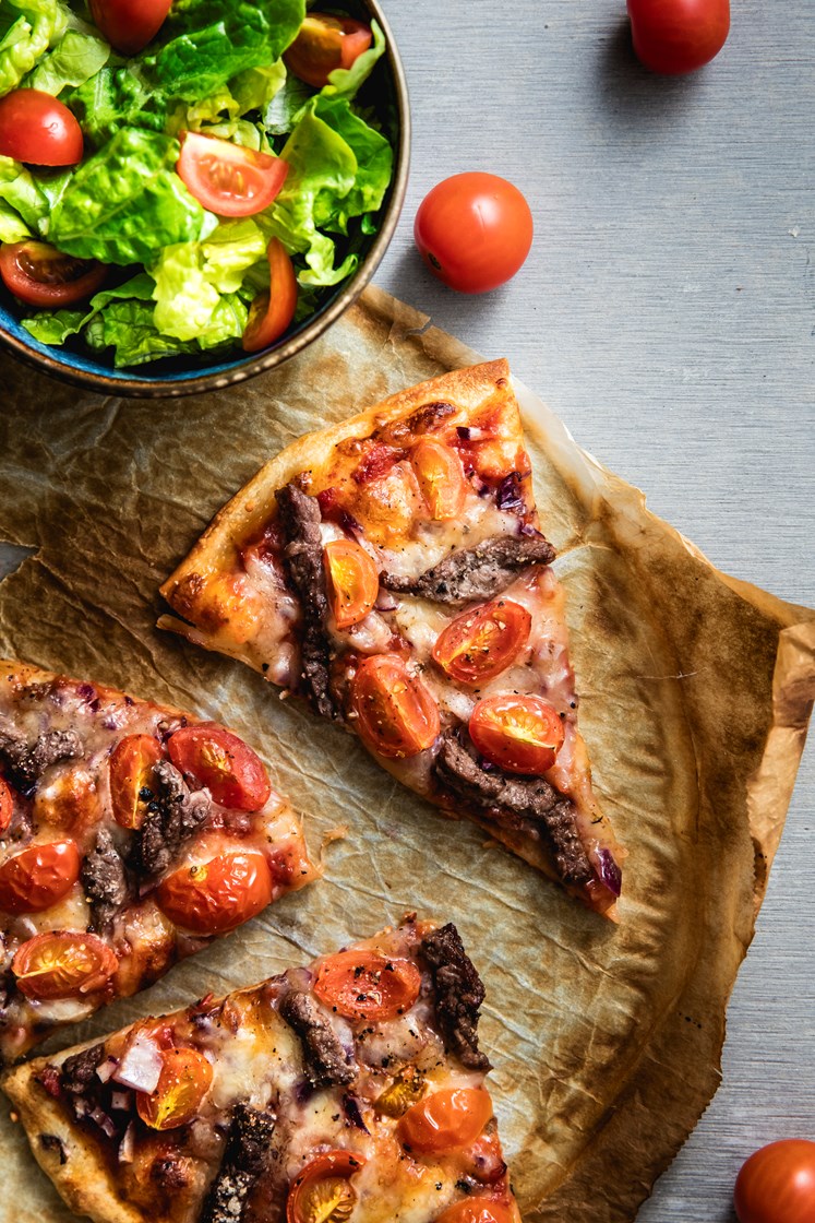 Pizza med biff, cherrytomater og mozzarella servert med frisk salat