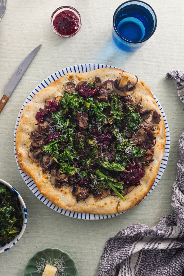 Hvit pizza med villhjortskav, sopp og sprø grønnkål, toppet med rørte tyttebær og lagret ost 